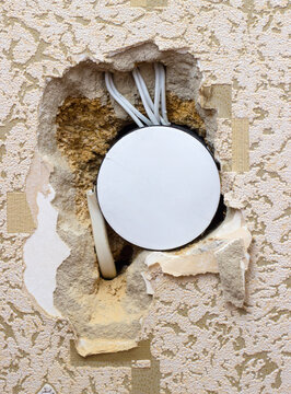 Damaged wall with exposed electrical wires and junction box under old wallpaper.