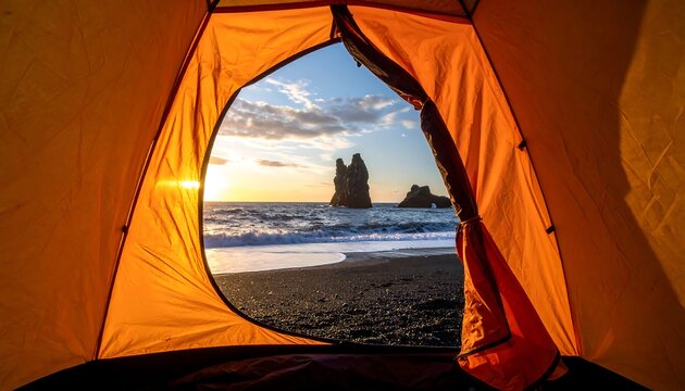 View from inside an orange tent shows a black sand beach with a sunset and rock formations in the ocean