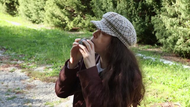 Mid shot of a young Caucasian woman wearing vintage clothes playing an ocarina ceramic flute. Park in the background. Ethnic music on a whistle toy