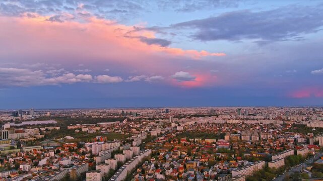 Bucharest, Romania - 15 April 2026: Aerial view of the city skyline and residential neighborhoods under a vibrant pink sunset sky with scattered clouds.