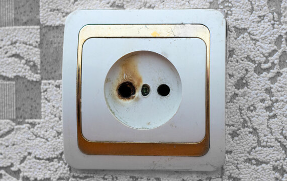 Burned electrical socket on a dirty wall. Fire hazard and faulty wiring concept.