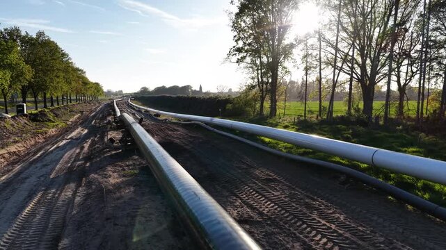 Construction of large metal pipelines along a rural path next to green trees