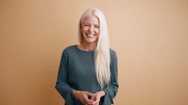 Joyful blonde woman expressing genuine happiness and laughing heartily. Cheerful and positive female model showing sincere emotions in a studio