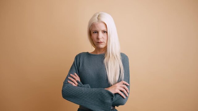 Serious middle aged woman with long blonde hair crossing her arms. Unhappy and resentful person standing with a defiant and angry expression
