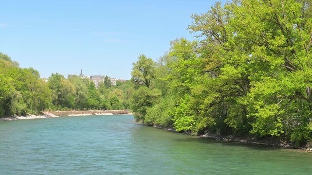 Serene turquoise river bordered by leafy trees under a clear blue sky, scenic nature landscape with calm water and spring foliage.