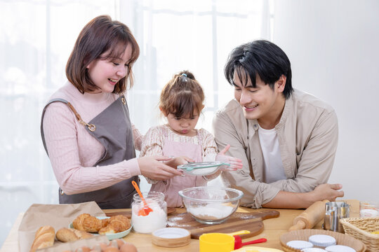 Family enjoys baking bakery together in the kitchen while using a laptop for recipes