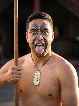 Portrait of Māori man performing haka with taiaha, fierce expression and traditional face tā moko. 