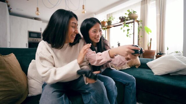 Happy young lesbian couple having fun while playing a competitive video game together. Cheerful women sitting on the sofa and enjoying their leisure time