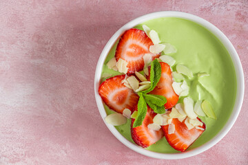 Green matcha yogurt served with sliced strawberries and almond flakes in a bowl. Top view with copy...