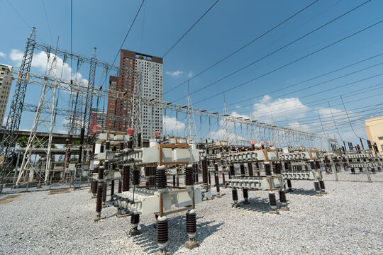Industrial Power Station with High Voltage Equipment under Bright Blue Sky and Urban Backdrop