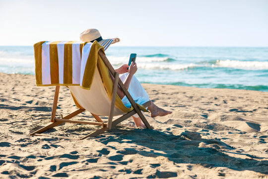 Woman using smartphone on beach chair with ocean view