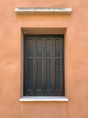 Fototapeta premium Traditional wooden window shutters on pastel orange stucco wall in Corfu Island, Greece.