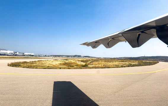 Athens international airport, Greece. Airplane wing view over taxiway and terminal buildings under blue sky
