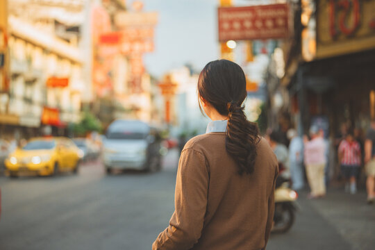 Back view of a young Asian woman with a ponytail looking and walking at the vibrant street of Bangkok Chinatown Yaowarat