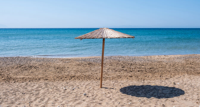 Straw umbrella on the sand of Komi Beach, Chios Island, Greece. Summer sunny day and calm turquoise sea.