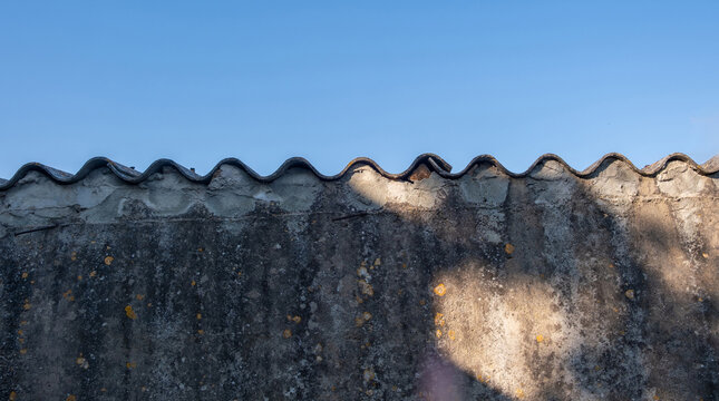 Weathered concrete wall with wavy corrugated top under blue summer sky