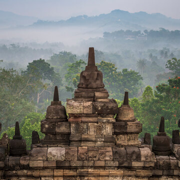 The unique Stupas of Borobudur Temple in Yogyakarta, during sunrise, overlookign a misty jungle landscape