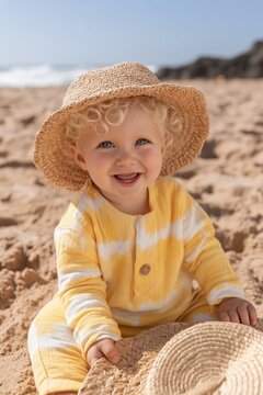 Smiling baby sitting on sandy beach wearing straw hat