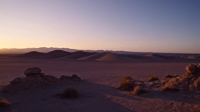 Desert sunrise revealing dunes and scrub brush under a clear, cloudless sky with sounds of footsteps