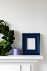 Naklejka premium Empty blue frame standing on mantel with candle and foliage