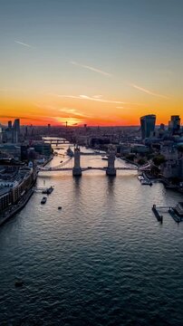Aerial hyperlapse sunset view of the illuminated Tower Bridge and City skyline of London, UK, with river traffic