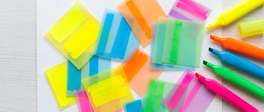 Colorful highlighters and transparent sticky notes scattered on a white desk surface