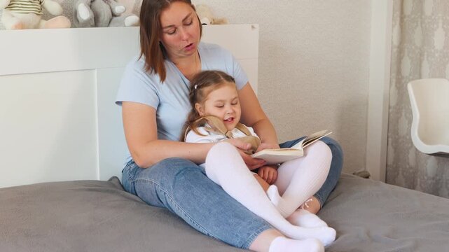 Caucasian mother supports her little girls learning through reading in a cozy bedroom. Childhood development and emotional communication concept.