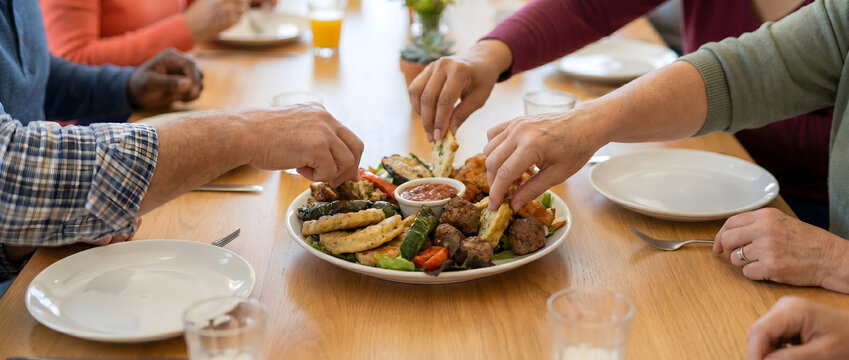 Multiple people gathered around a wooden table sharing a healthy platter of vegetables, meats, and dips