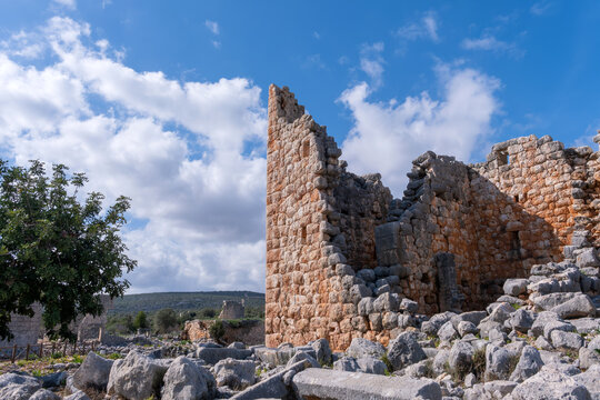 Ancient stone ruins of a sun-drenched fortification wall stand against a clear blue sky in a Mediterranean landscape. This majestic archaeological site evokes history and heritage. Mersin, Turkey.