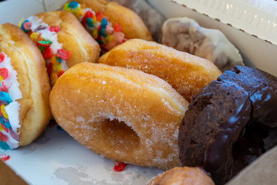 Close-up of a delectable assortment of fresh donuts, featuring colorful sprinkle-covered, classic sugar-dusted, and rich chocolate-glazed varieties in a bakery box, perfect for a sweet indulgence.
