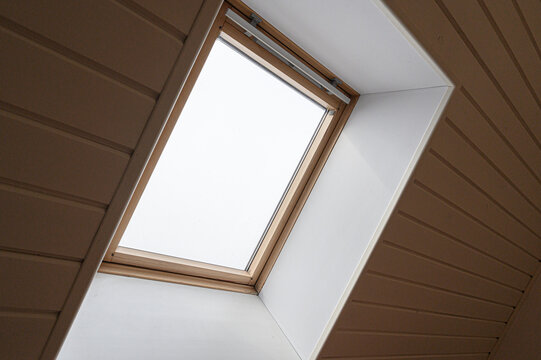 rectangular skylight with a light wooden frame set into a sloped ceiling. Beige paneling surrounds the window; frosted glass diffuses natural light softly.