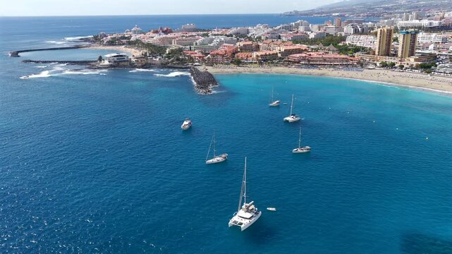 Aerial View of Playa de las Americas and Los Cristianos; Sailboats Anchored in Turquoise Bay with people swimming at the beach