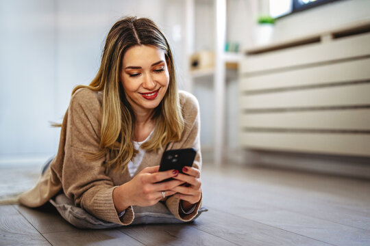 Smiling young female using mobile phone app playing game, shopping online, ordering delivery