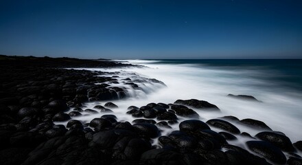 Fototapeta premium Long exposure of ocean waves crashing against black volcanic rocks at night.