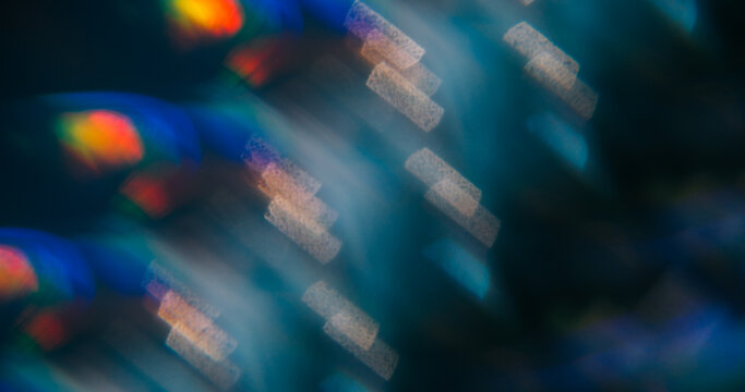 Night bokeh prism. Reflection glow. Color striped light on defocused black background. Vibrant abstract blue violet orange twinkle luminosity.
