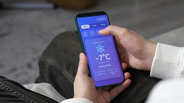 Planning for a cold winter day. Close-up of a person tracking heavy snow and freezing temperatures on a mobile application. Useful for outdoor planning, winter sports ads, and climate awareness