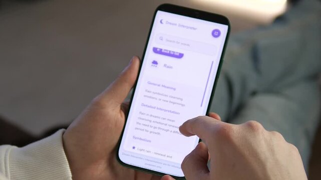 Close up of man using Dream Interpreter mobile app to analyze symbols. Close-up of hands scrolling through dream symbols and meanings like Rain. Perfect for technology reviews, app marketing, and