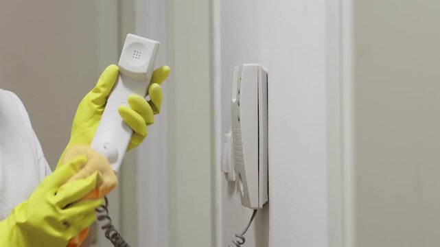 Housewife in rubber gloves wipes intercom handset with wet rag. Cleaning service. Close up of hands