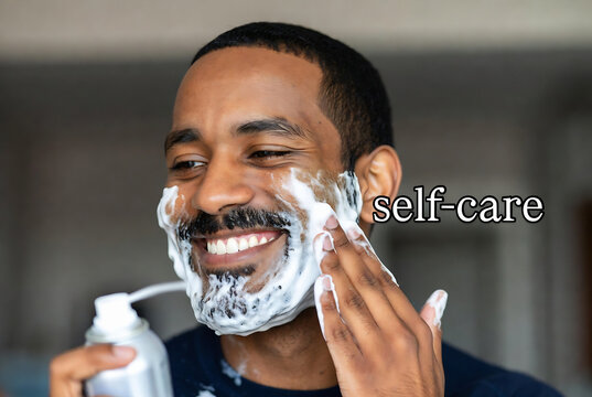 Subject: A Black man. Action: He is applying shaving foam to his face. Setting: An indoor bathroom.