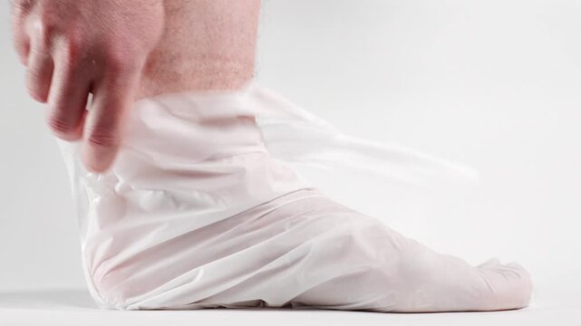 Side view of man unties cosmetic sock and takes out foot with peeling skin. Effect of skin renewal with acidic pedicure cosmetics. Close-up, white background