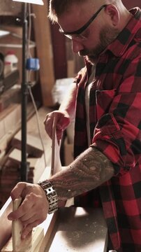 Vertical video. Joinery work. Cutting wood. Male carpenter in safety glasses pushing plank with press pad on professional power electric machine.