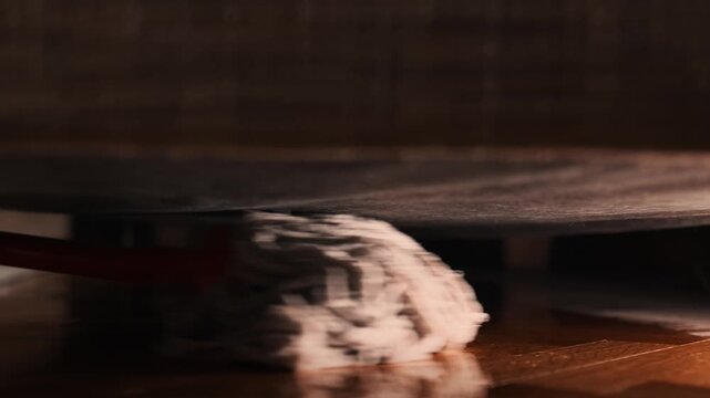 Professional cleanup. Wet mop washing and wipes dust under slit between sofa and floor, close up. Cleaning service. Low angle view. Tracking right shot