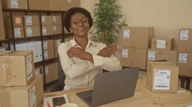 Woman at packing desk with laptop and cardboard packages, arms crossed and smiling, shipping labels visible in warehouse; entrepreneurship resilience confidence.