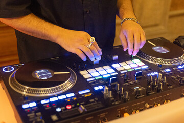 Obraz premium DJ mixing music on professional controller with illuminated pads in nightclub environment.
