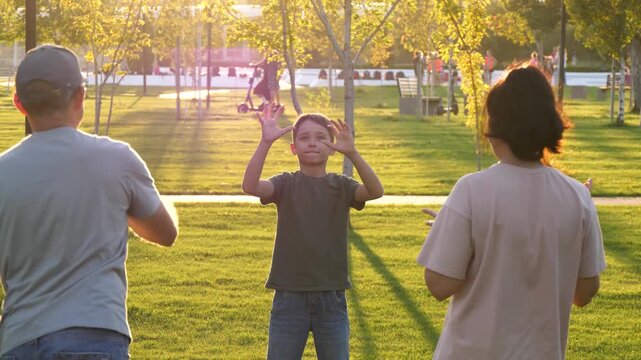 Happy family playing American football together in park at sunset. Mother, father and son pass ball and smile in warm golden light. Concept of bonding, active lifestyle and joyful childhood outdoors.