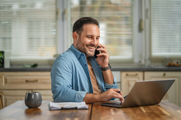 Obraz premium Smiling man working from home talking on phone