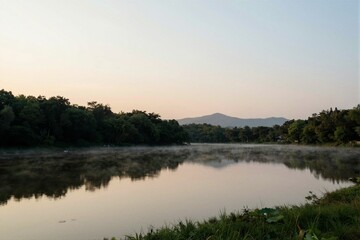 Fototapeta premium Calm river reflecting trees and distant hills at sunrise
