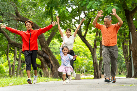 Front view of Asian family with young father, mother, daughter and grandfather express happy by raise up their hands for the success of running along the road in public park or garden together.