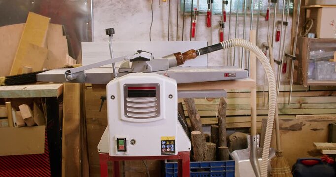 Woodworking process. Joiner service. Man push plank in thickness machine preparing material for furniture making in garage interior.