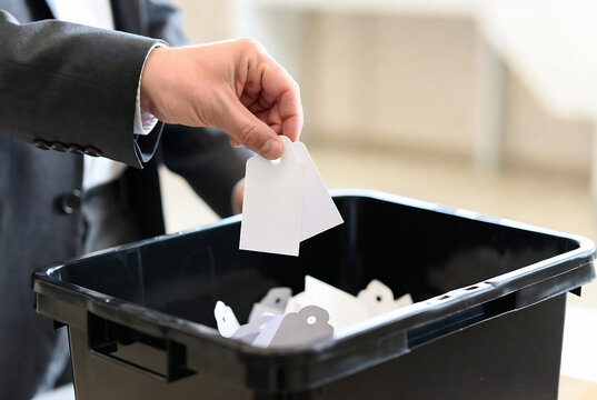 A hand is discarding a ballot into a voting box. It appears to be a polling place or election location.